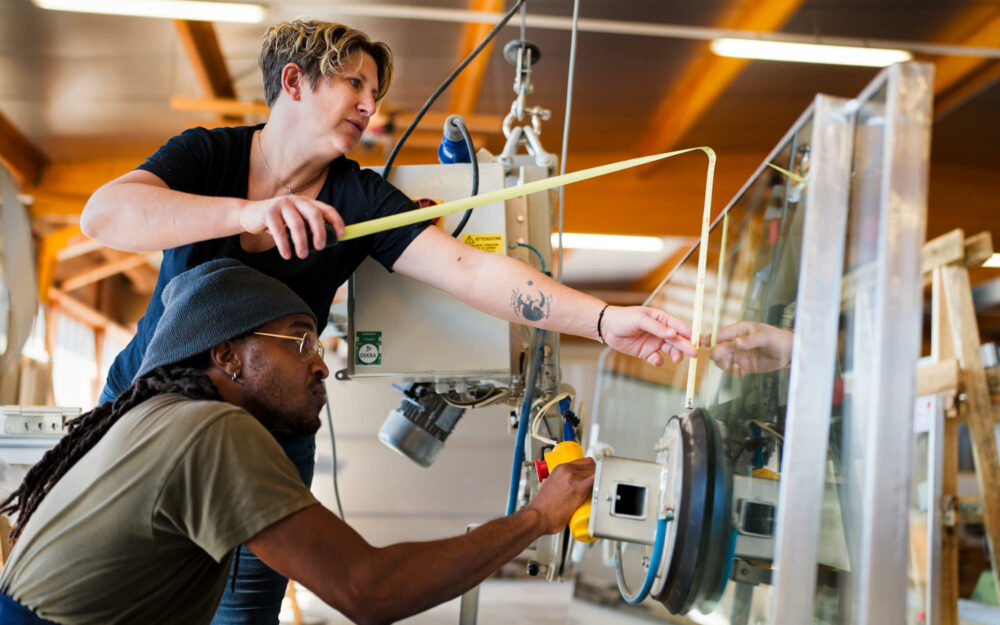 Ouvriers prenant des mesures pendant l'installation de vitres sur un encadrement de fenêtres en bois.