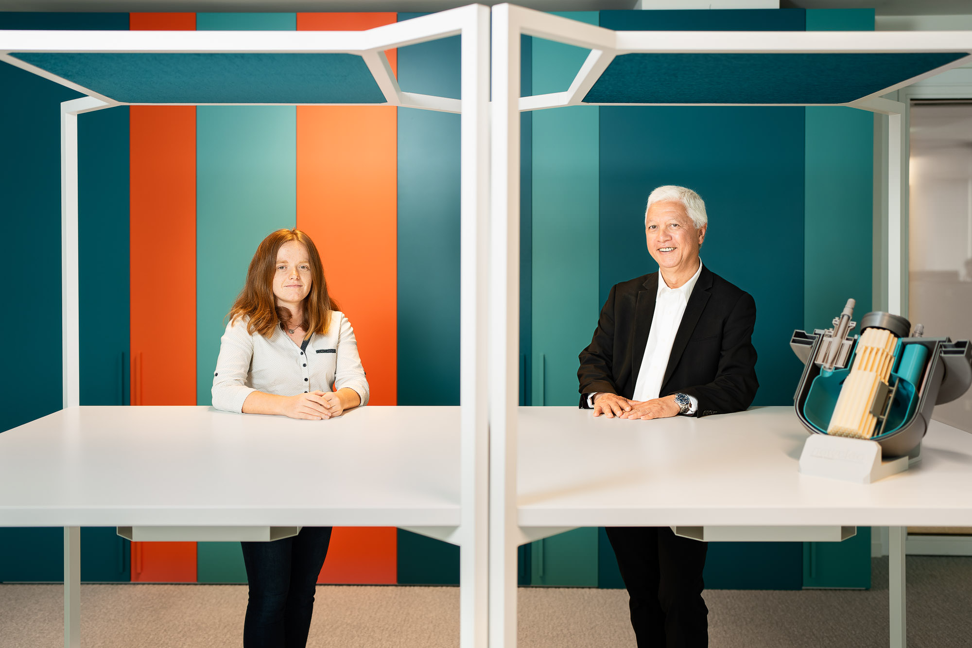 Portrait en entreprise à Lyon : portrait duo de deux personnes assises à une table, fond graphique